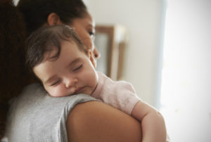 A mother holds her sleeping baby over her shoulder.