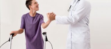 A child using a walker laughs and shakes hands with his doctor.