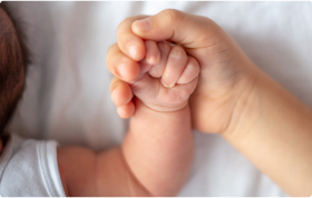 A baby’s hand is gently held by an adult’s hand.