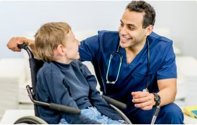 A cerebral palsy specialist smiles while interacting with a child in a wheelchair during a check-up.