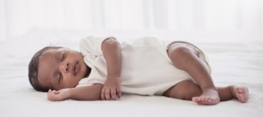 A baby lies on its side on a soft white surface and white background.