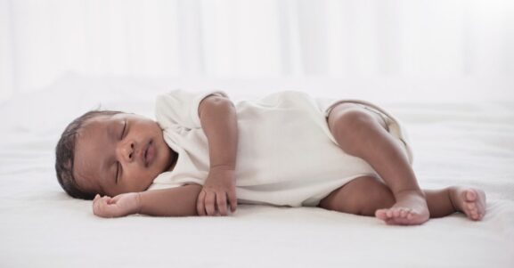 A baby lies on its side on a soft white surface and white background.